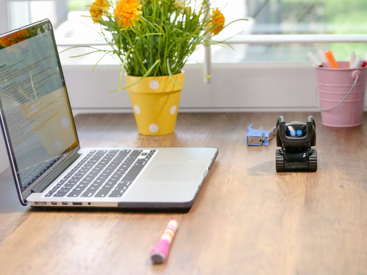 services-01 Stylish workspace featuring a laptop, toy robot, and vibrant flowers in natural light.